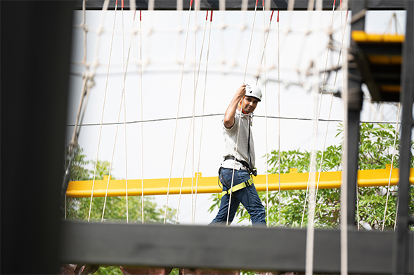 Guest navigating obstacles and looking at camera on rope course at Roadies Rostel ARC Resort