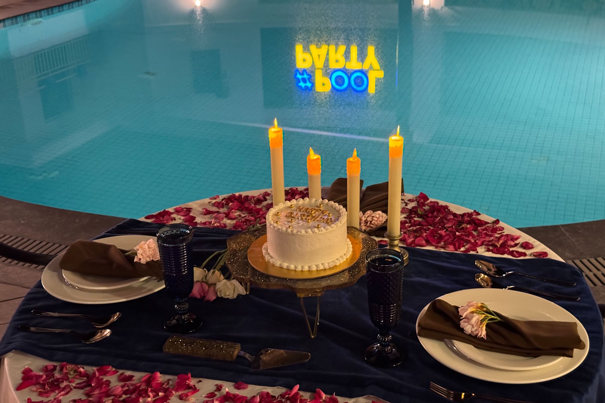 Romantic poolside dinner setup with cake and candles at Roadies Rostel ARC Resort