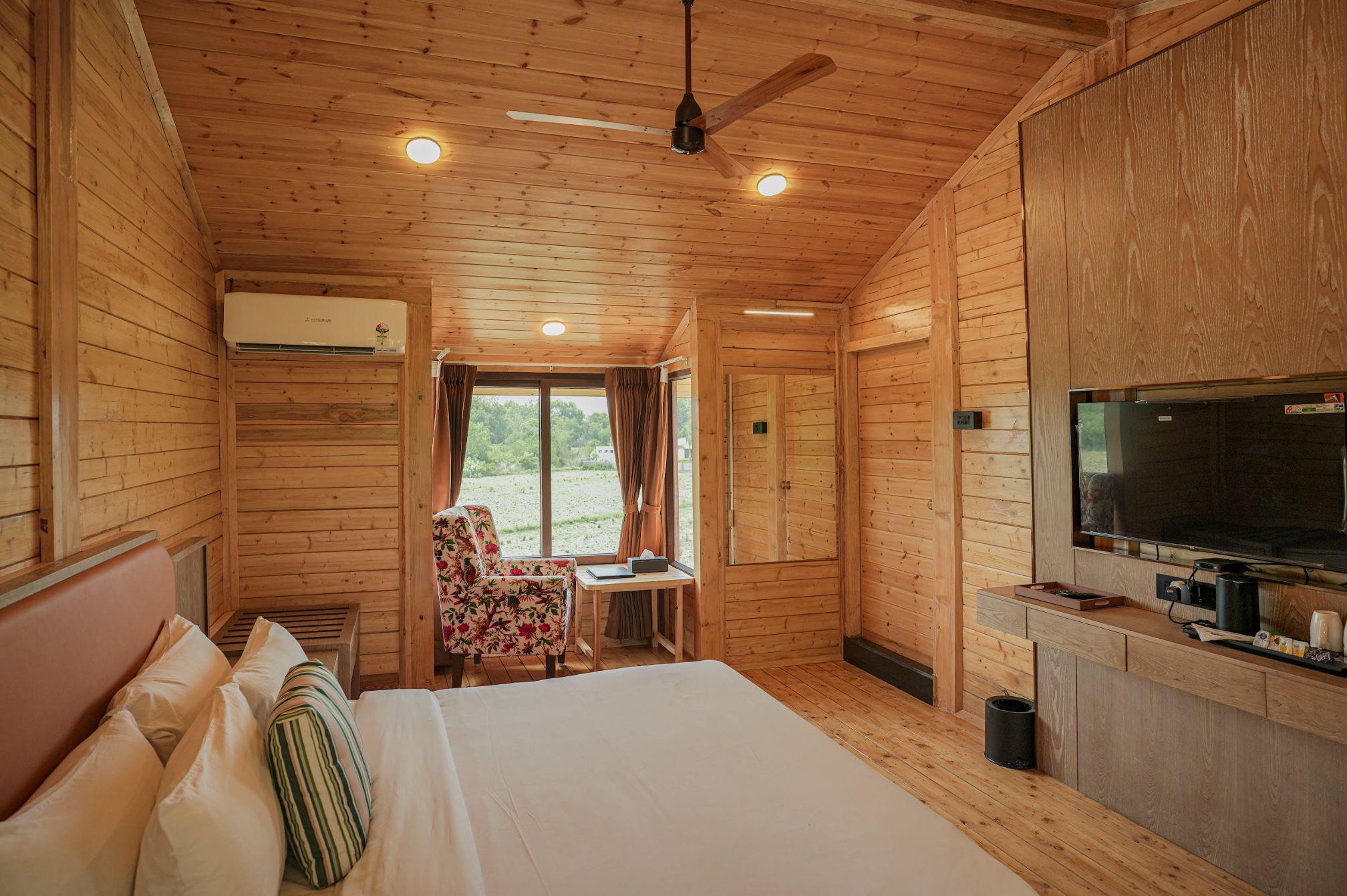 Spacious wooden cottage room interior with natural light at Roadies Rostel ARC Resort, Ahmedabad.