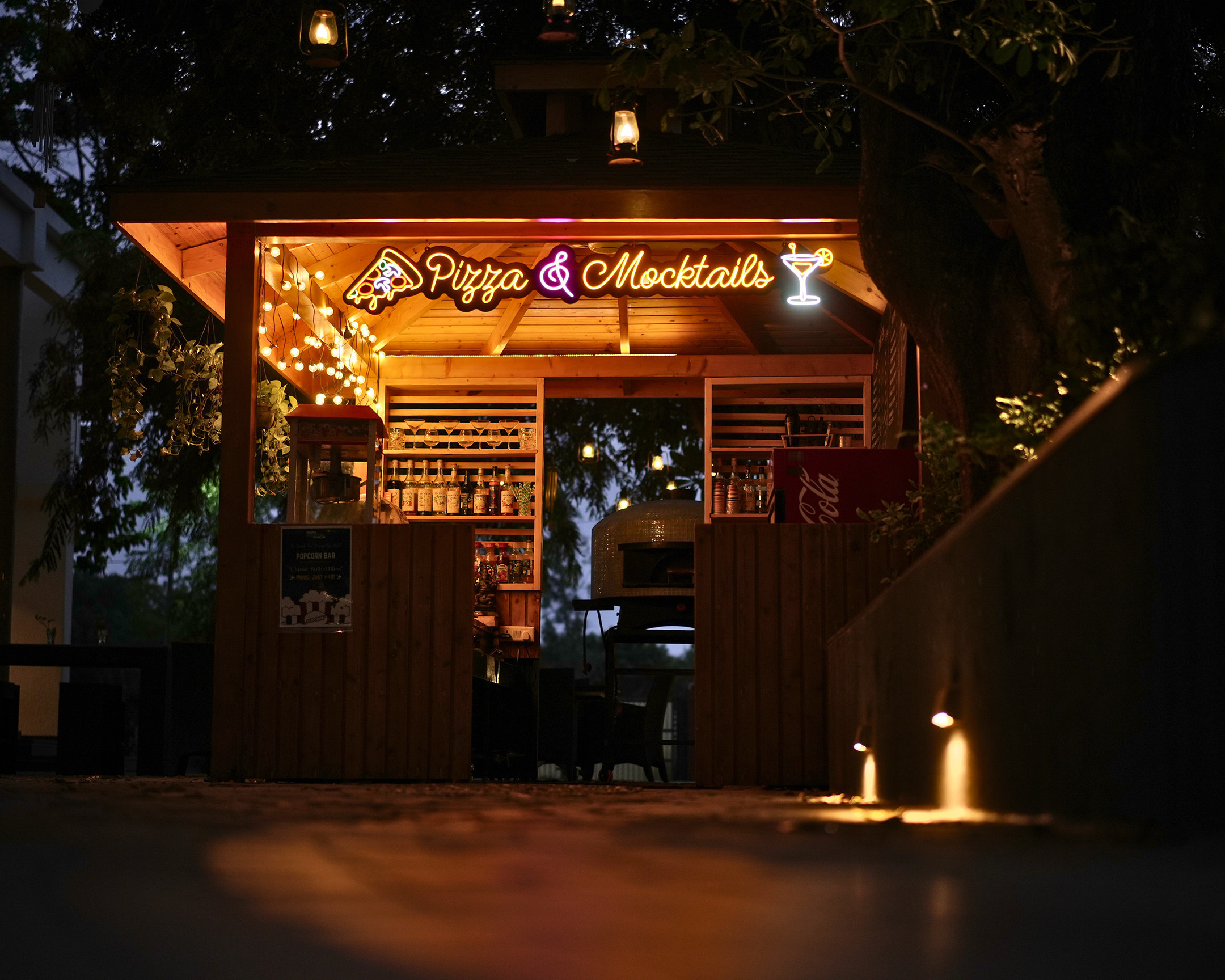 Nature-inspired wooden mocktail bar setup at The Nest, nestled in greenery at Roadies Rostel ARC Resort Ahmedabad – a perfect outdoor spot for refreshing drinks near Ahmedabad.