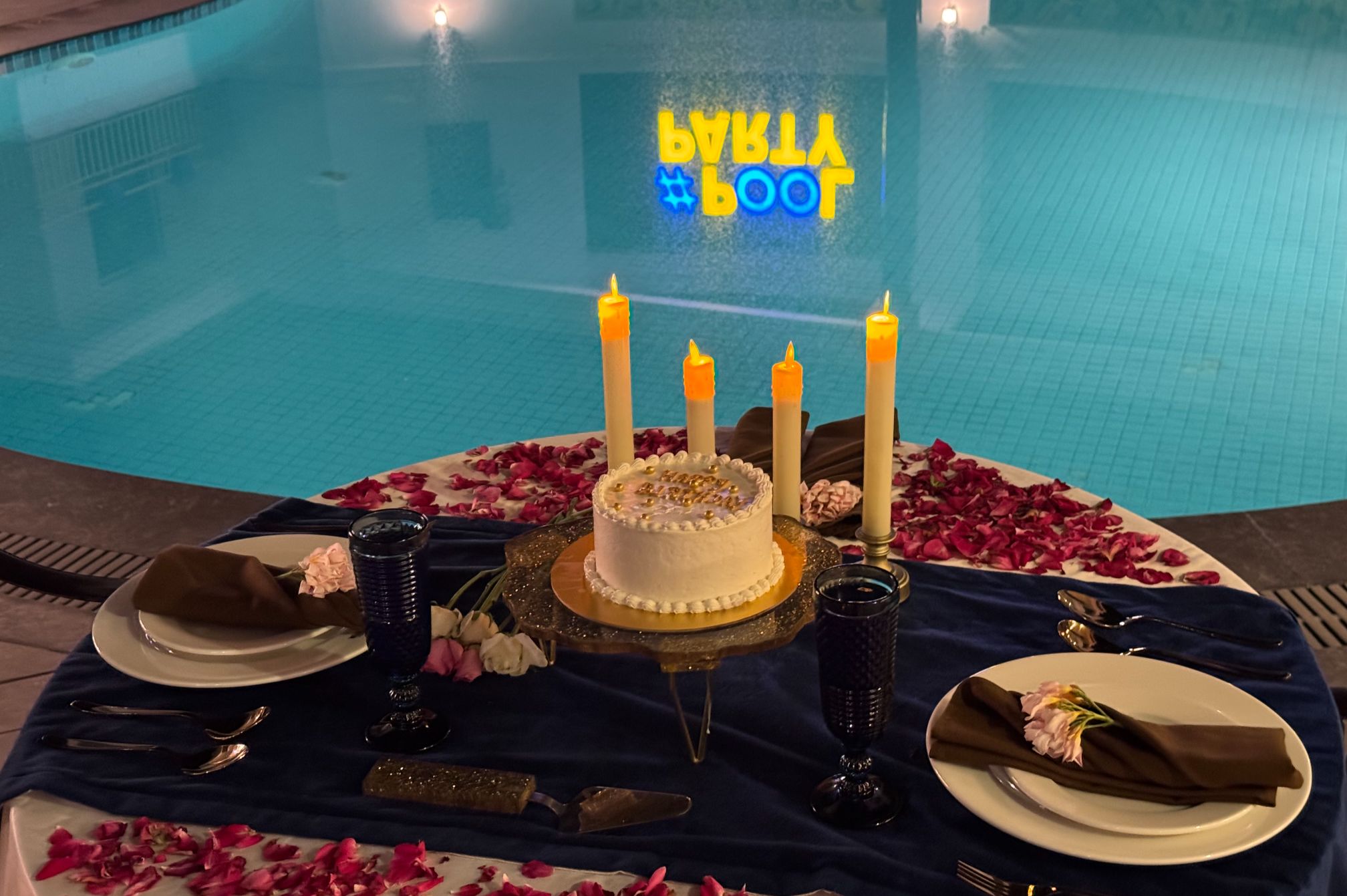 Celebration cake and candlelight dinner setup beside the illuminated pool
