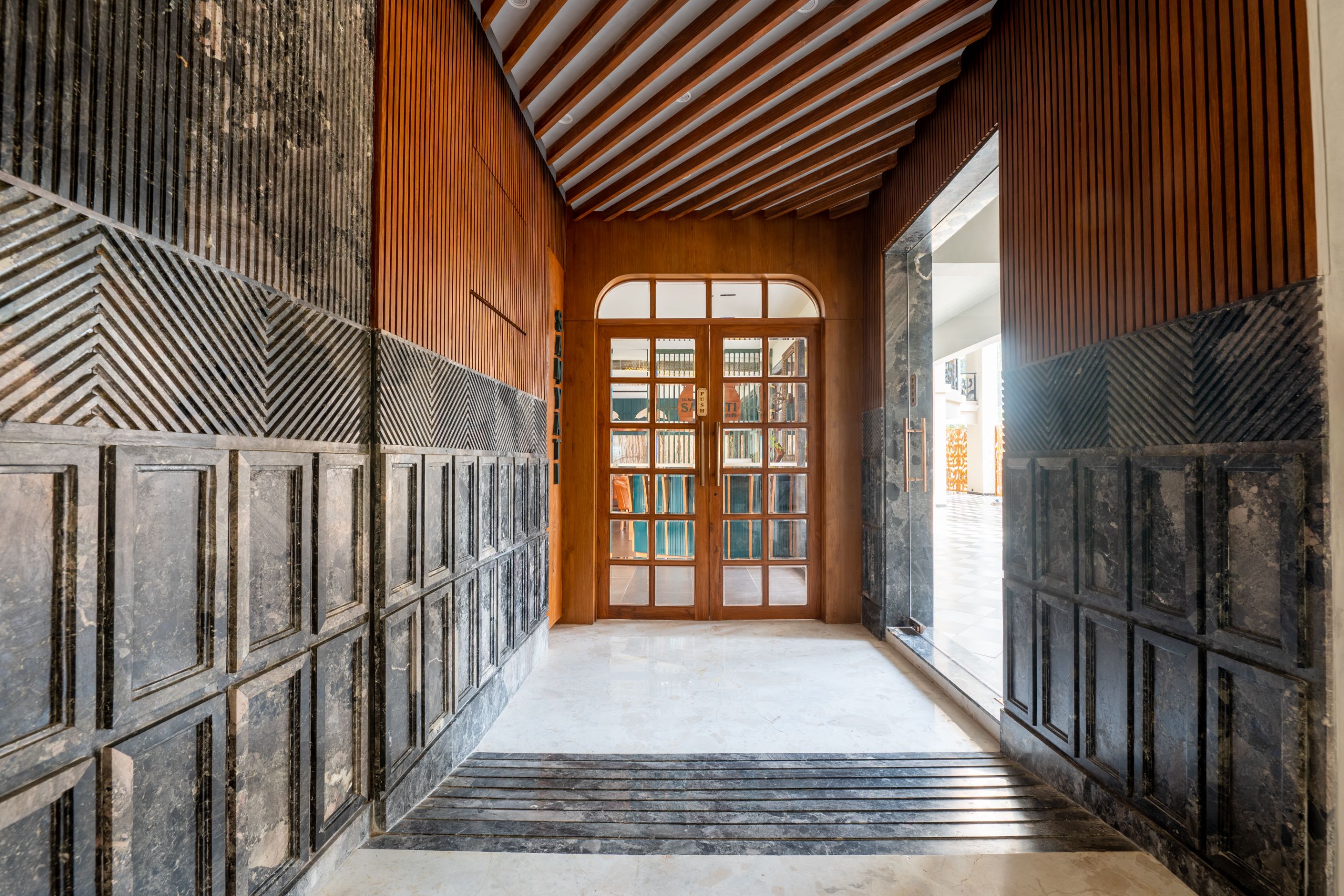 Stylish corridor with wood paneling leading to a glass door at Roadies Rostel ARC Resort near Ahmedabad