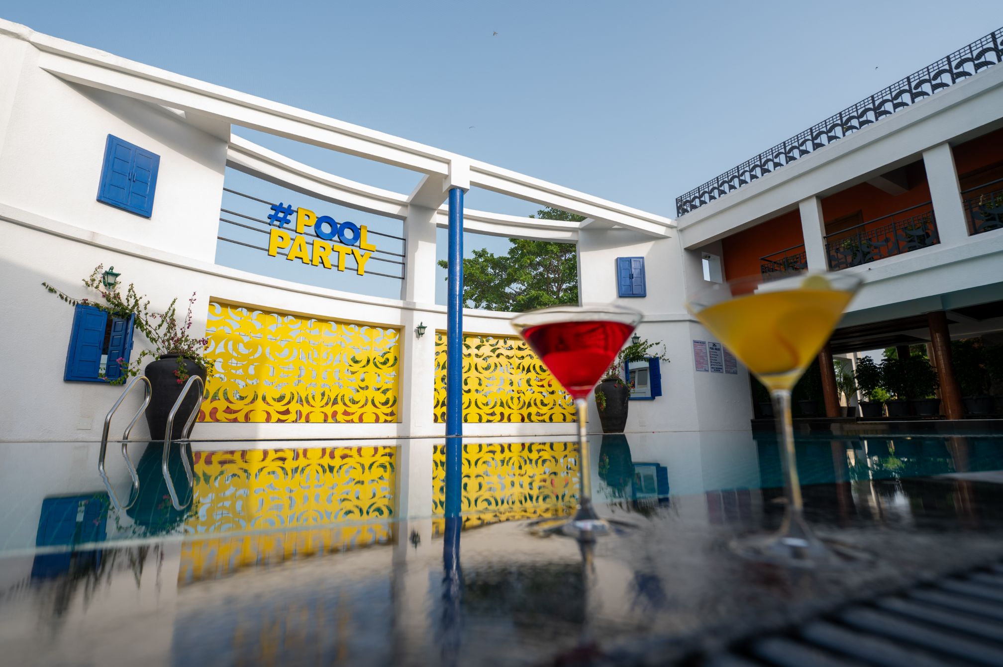 Colorful drinks by the pool with reflections of the pool party sign at Roadies Rostel ARC Resort